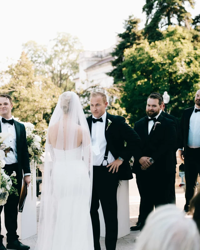The groom takes in the bride as she arrives at the altar, groomsmen grinning behind him