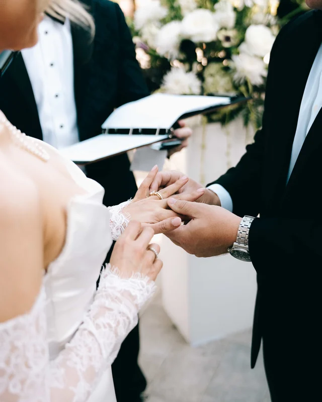The bride slides the band onto the groom's finger over the officiant's open folio