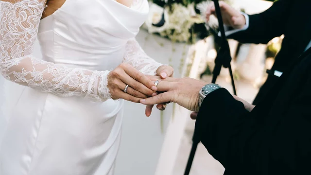 The groom guides a ring onto the bride's finger, her lace sleeve gathered at the wrist