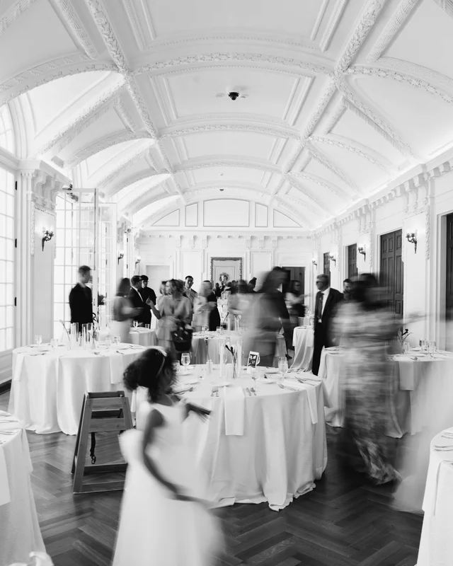 Long-exposure black and white of the reception room, guests blurring into motion beneath the barrel-vaulted ceiling