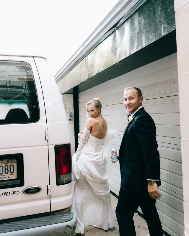 The couple slips down a back alley past a white van, the bride glancing over her bare shoulder