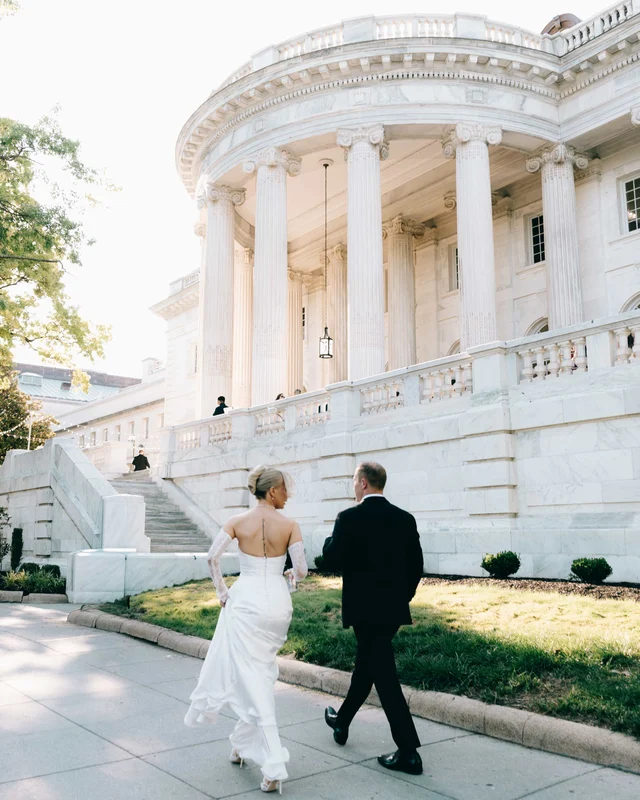 The newlyweds climb the lawn toward the great rotunda portico in low golden light