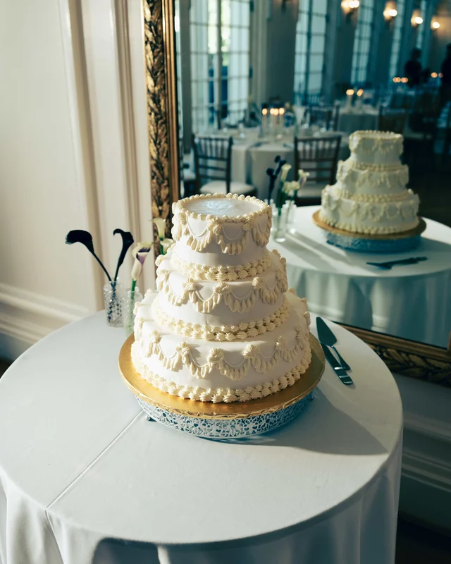 The tiered buttercream cake with piped swags doubled in a gilt mirror, calla lilies at its side