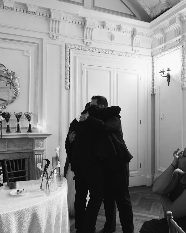 A three-way embrace after the toasts, a seated guest wiping her eyes at the edge of the frame