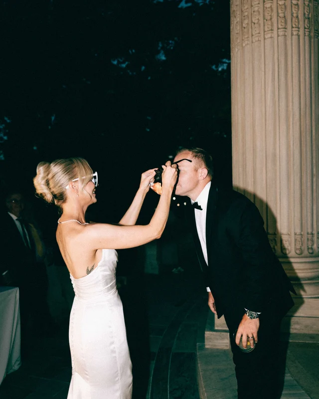 In white cat-eye sunglasses, the bride fits a dark pair onto the laughing groom's face at night