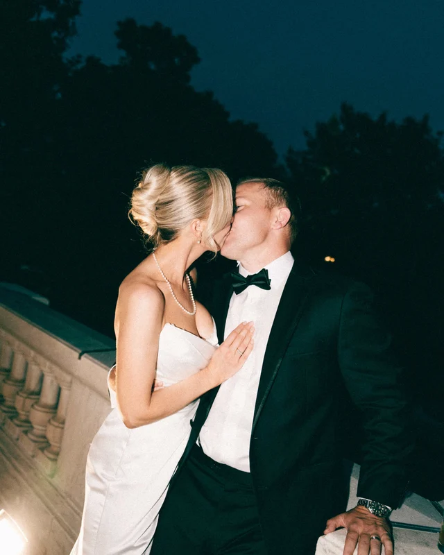 A flash-lit kiss against the ink-blue night sky, her hand flat on his lapel