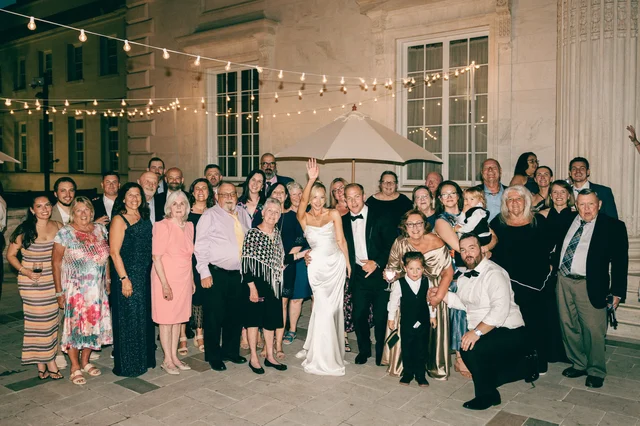 The whole dance floor gathers around the couple for a string-lit group portrait at night