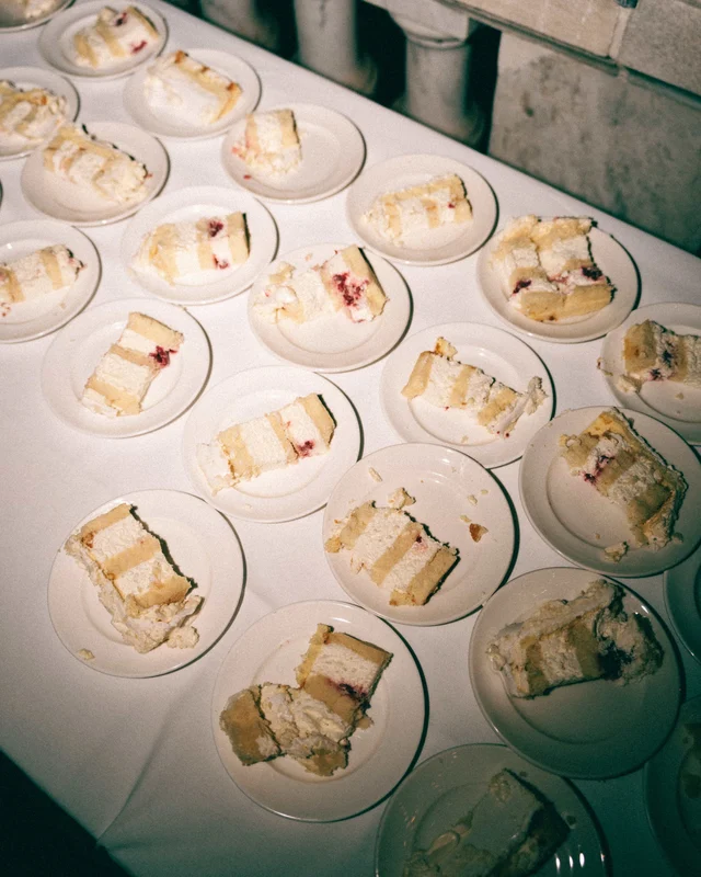 Slices of cake with jam-striped layers laid out on dozens of white plates