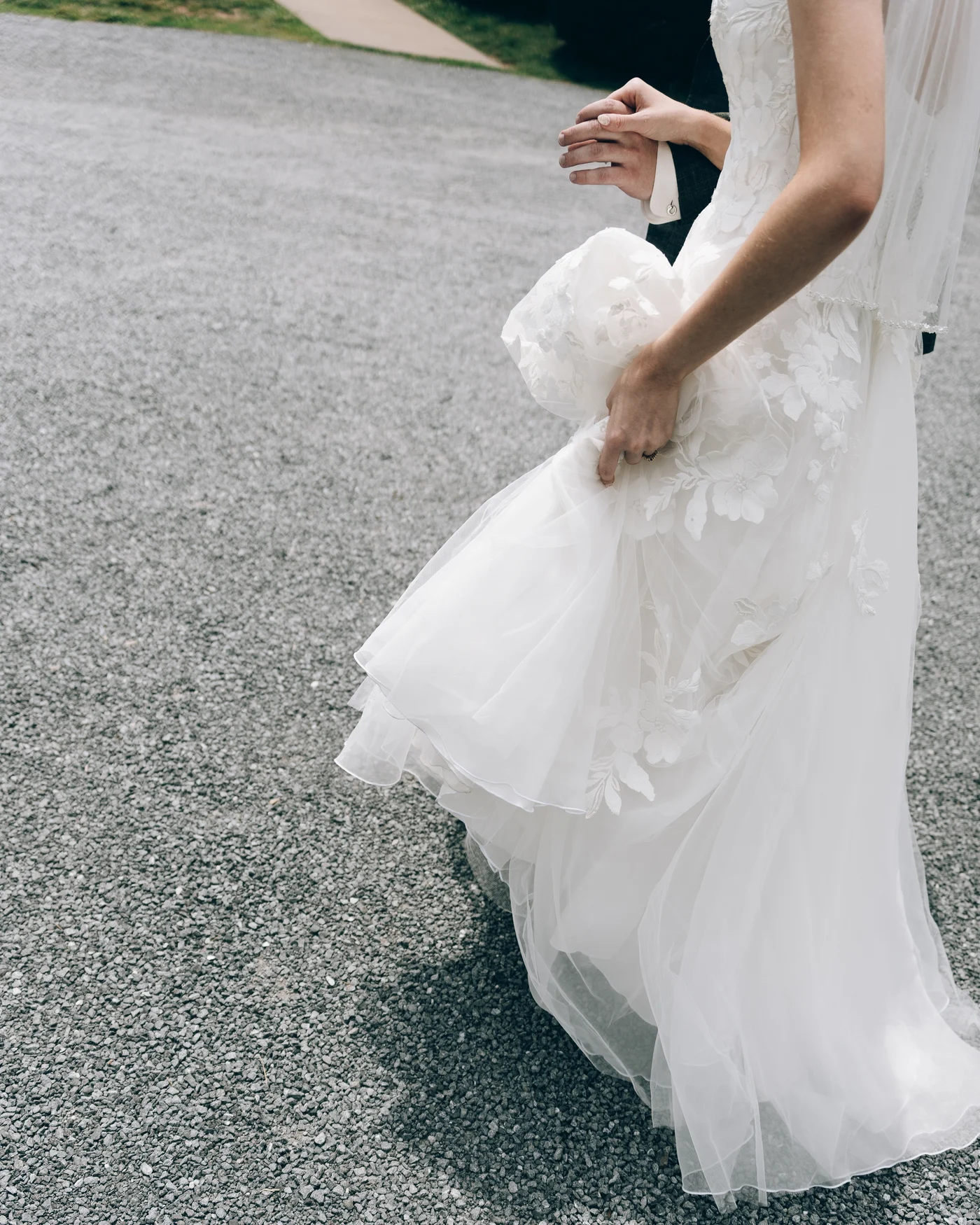 The bride's gown and train trailing across the gravel drive