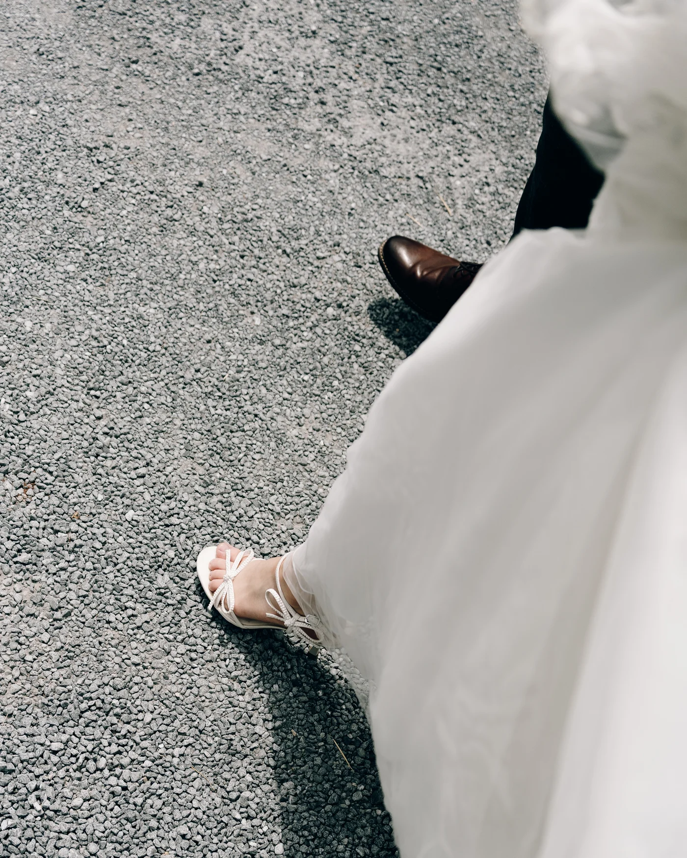 The hem of the bride's gown and her shoe on the gravel