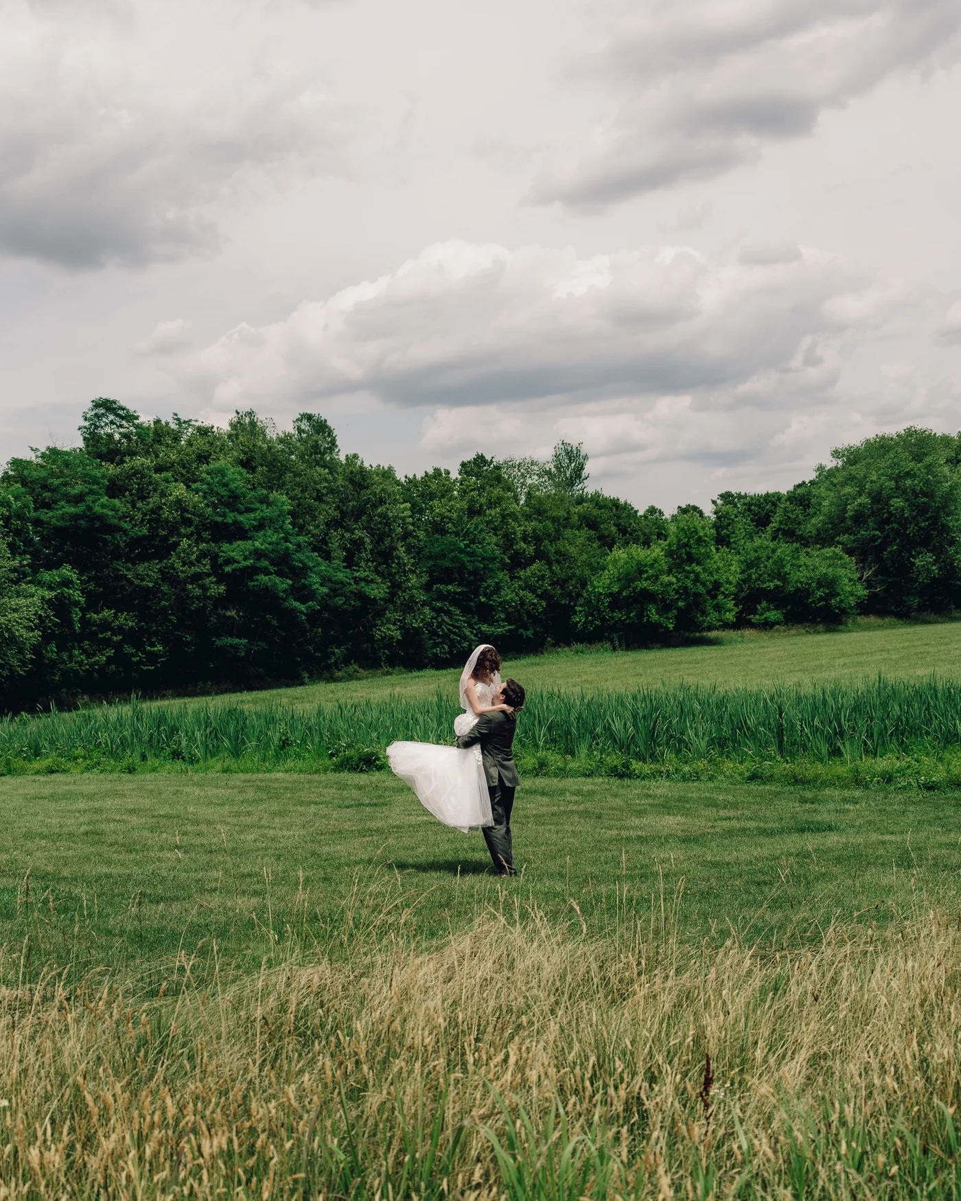 The groom lifting the bride off her feet in the long grass at the top of the property