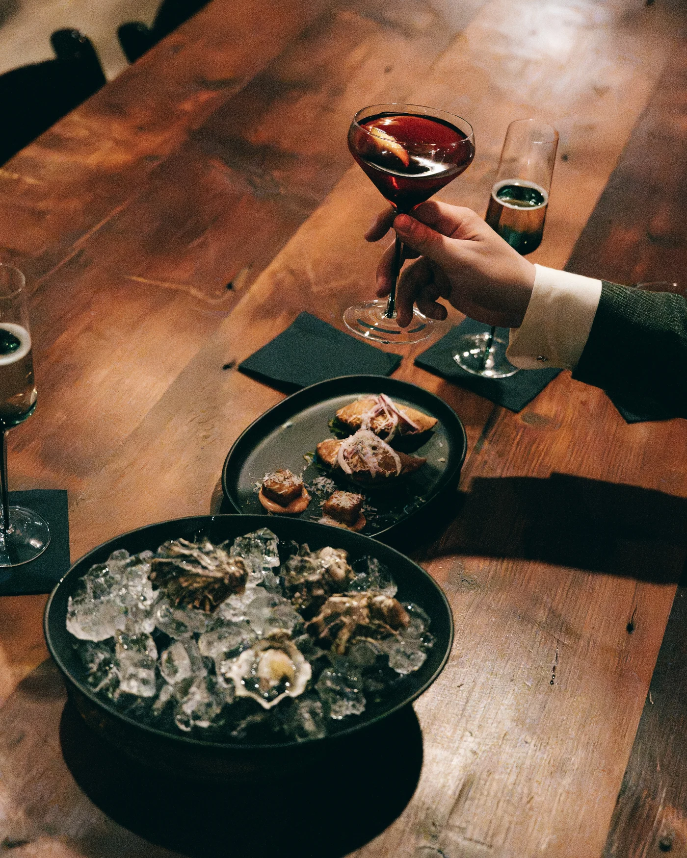 A coupe glass raised over trays of oysters on a dark wooden table