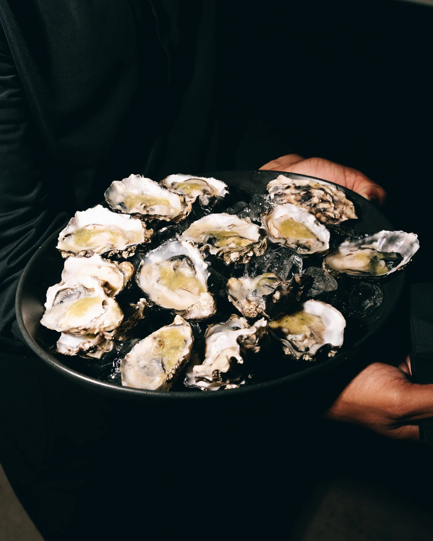 A tray of oysters on ice held up in the dark