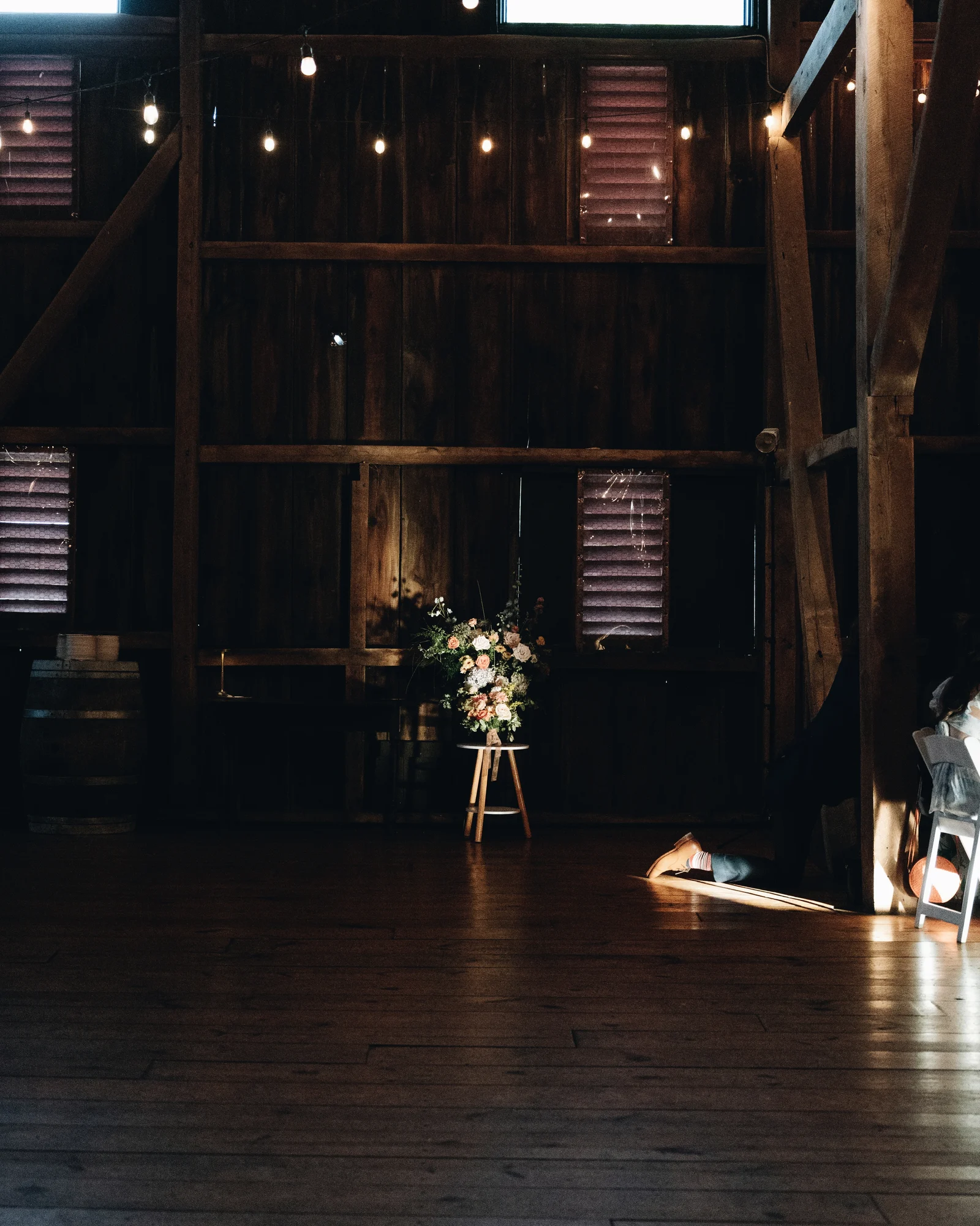 The empty barn floor at night, a single arrangement of flowers on a stool in the light