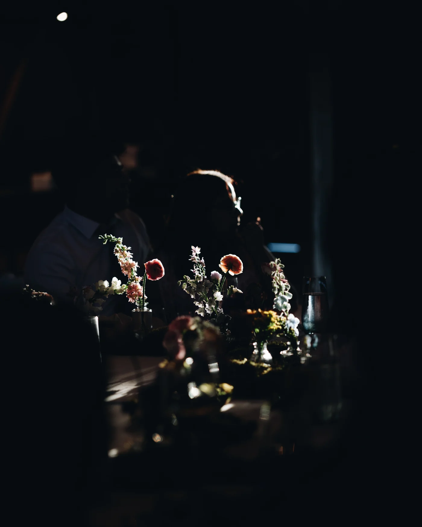 Wildflowers on the table in near darkness with guests behind them