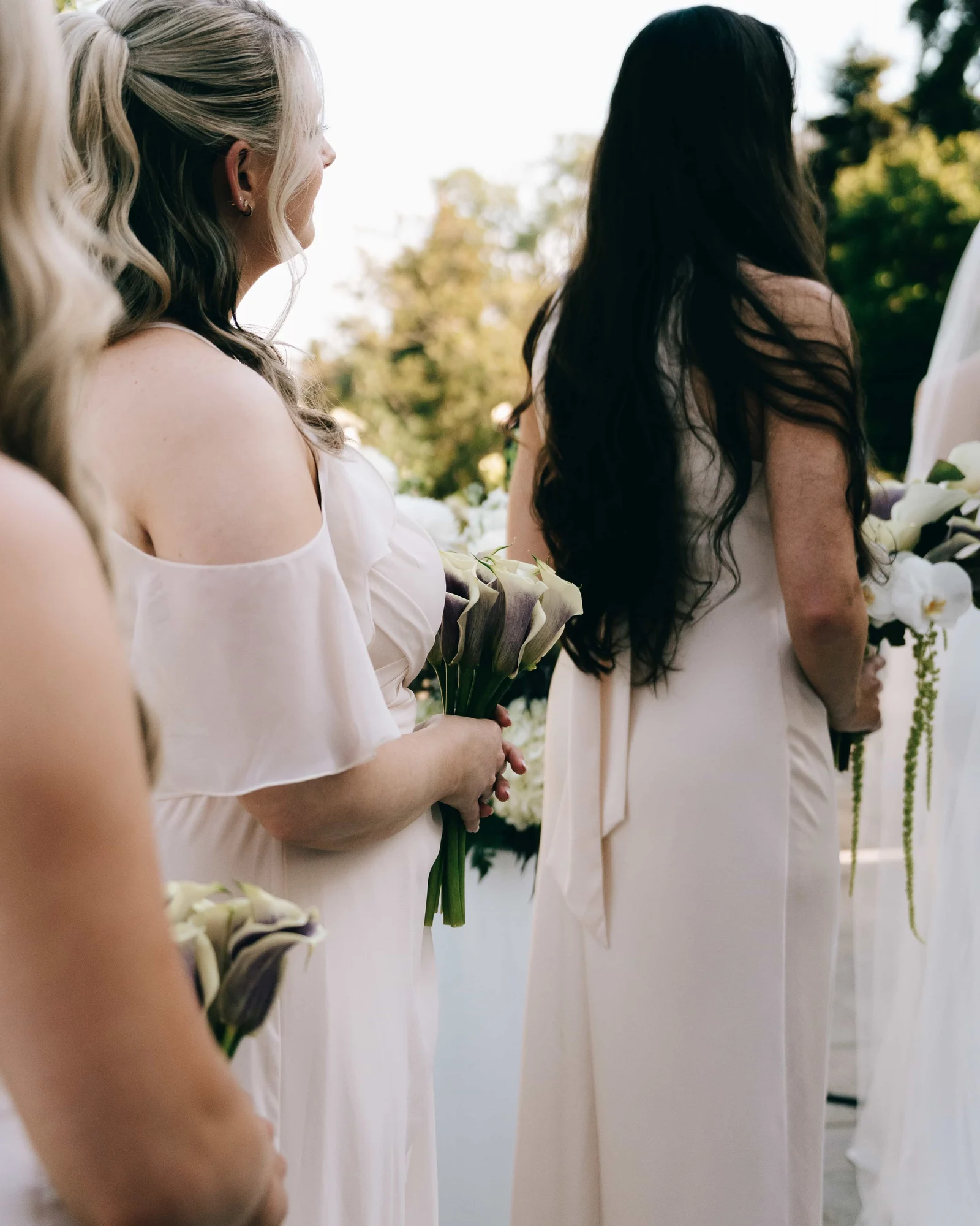 Bridesmaids holding bouquets of purple and white calla lilies, an orchid bouquet at the edge of the frame