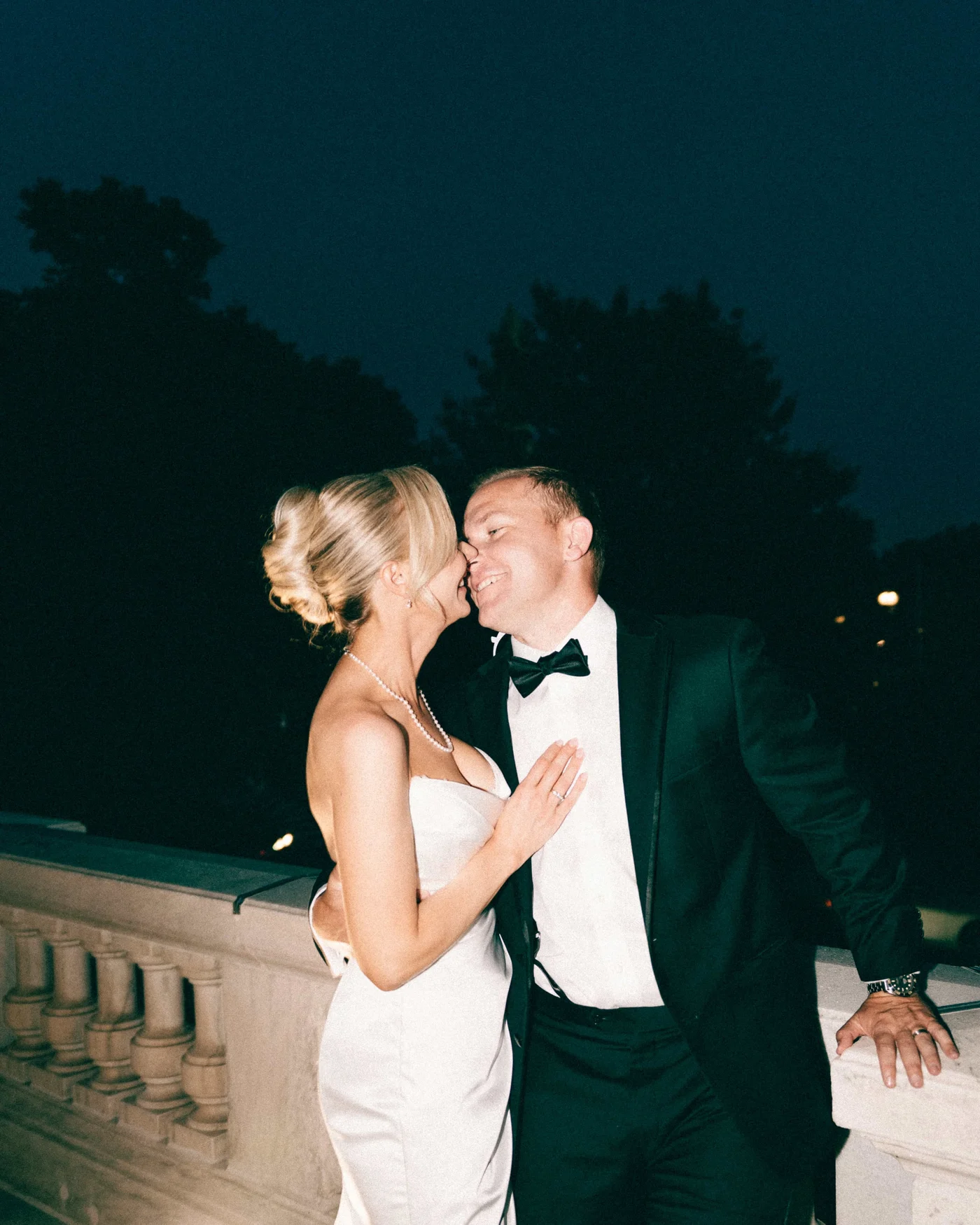 Nose to nose at the balustrade after dark, her hand resting flat on his chest