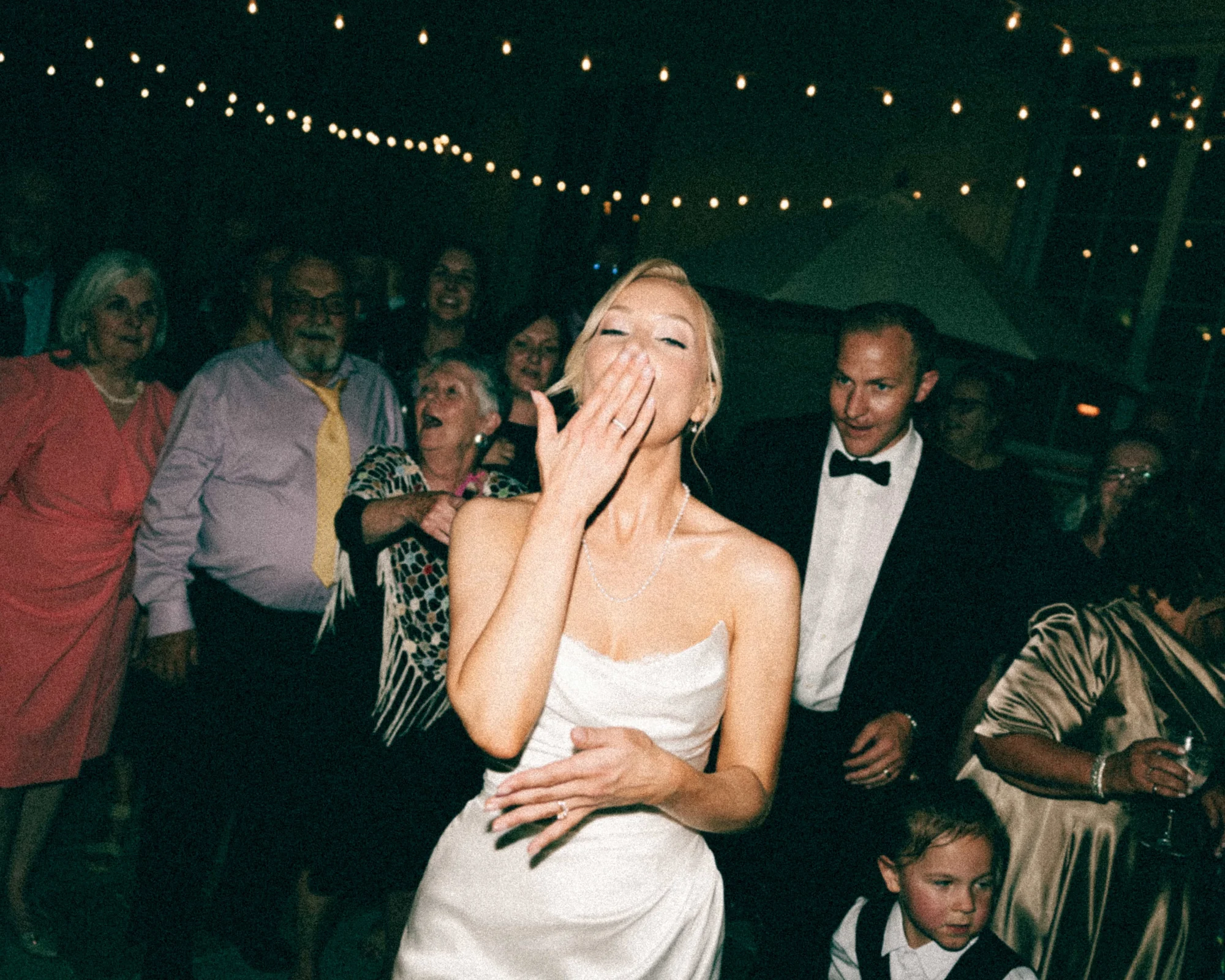 The bride blowing a kiss under the string lights, the whole dance floor lit up behind her