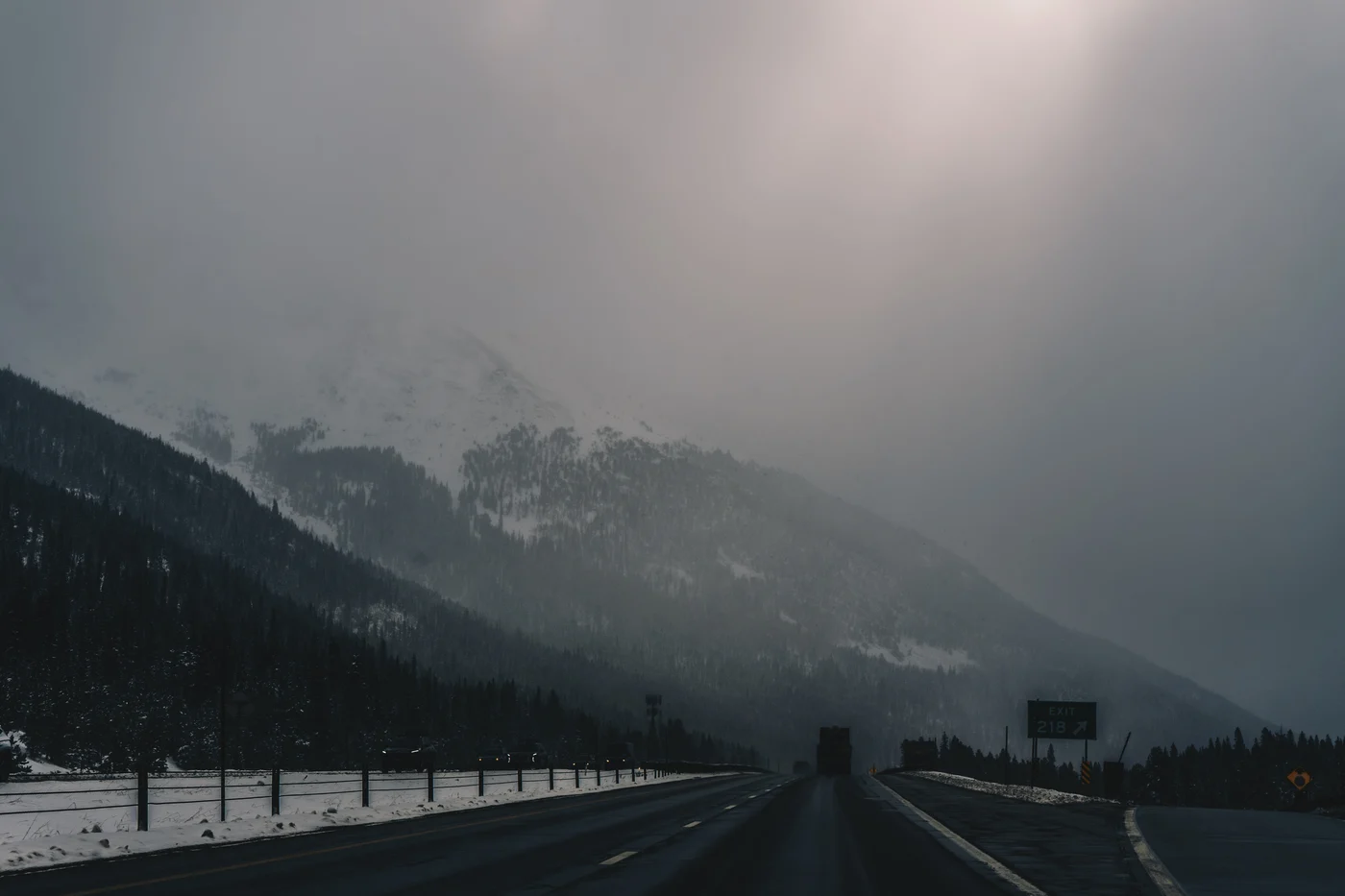 A truck far ahead on a wet interstate, a snowy mountainside dissolving into fog