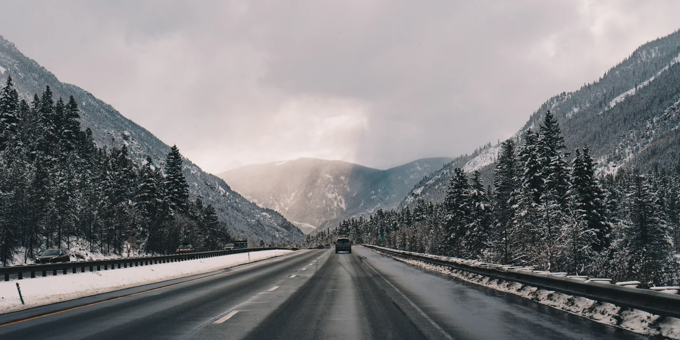 A straight highway running between snowy evergreen slopes toward sunlit peaks