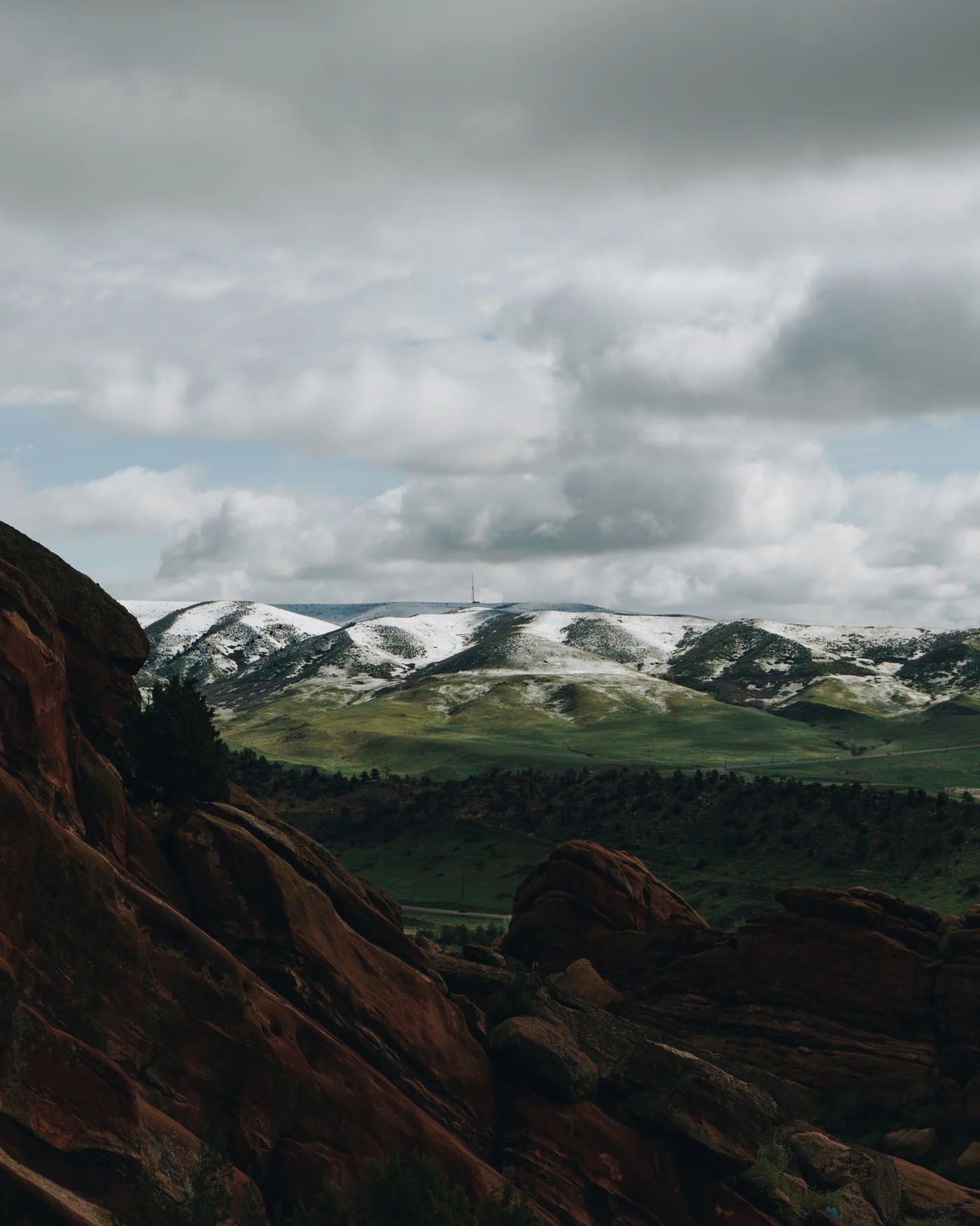 Red rock fins in shadow before green hills striped with fresh snow
