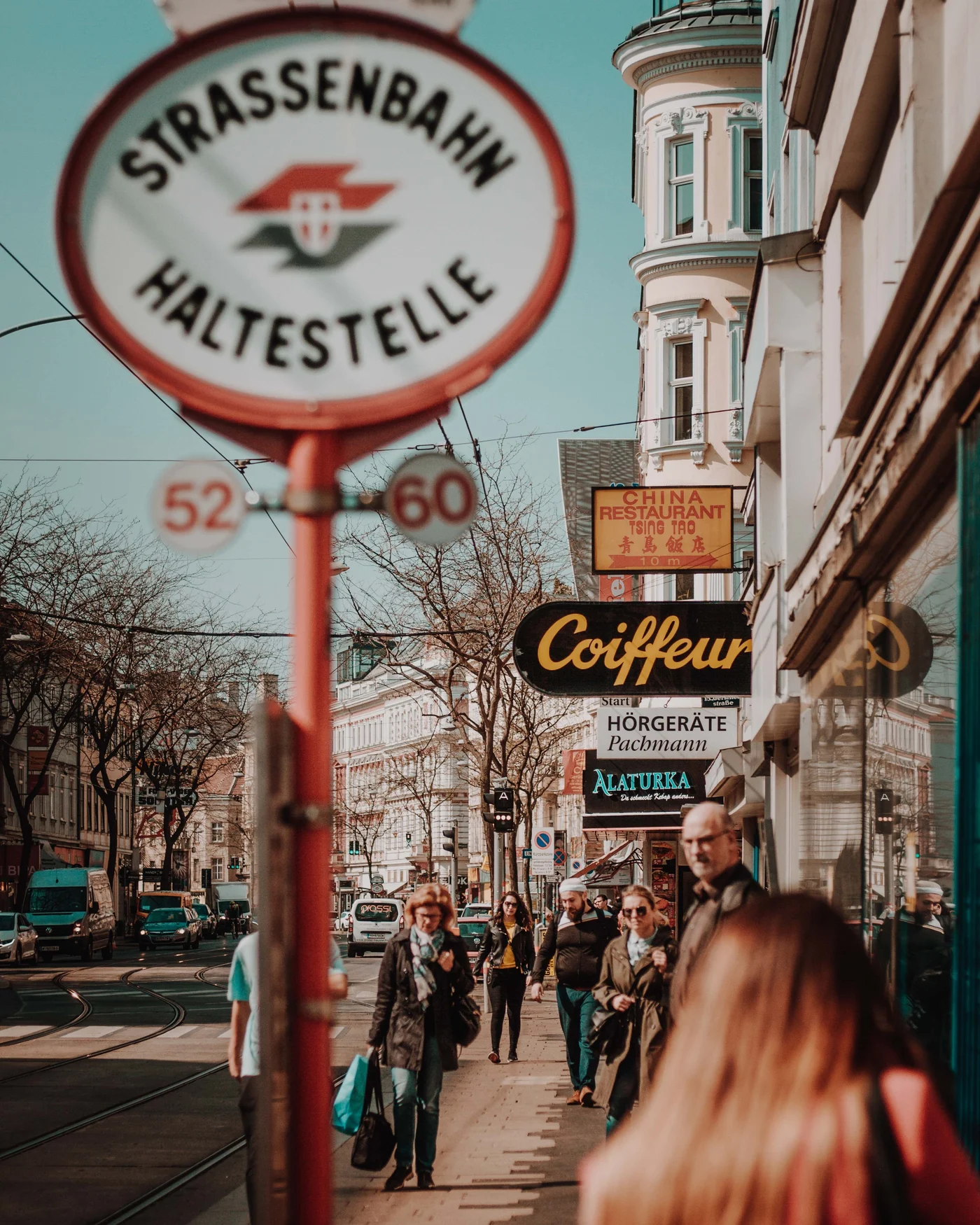 A tram stop sign hanging over a busy Vienna shopping street in spring sun