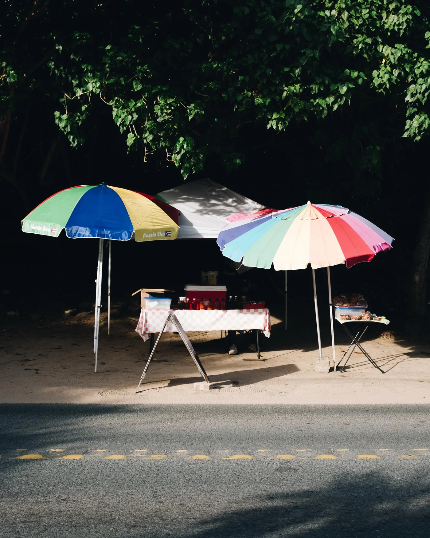 A roadside stand shaded by three bright beach umbrellas, one printed Puerto Rico