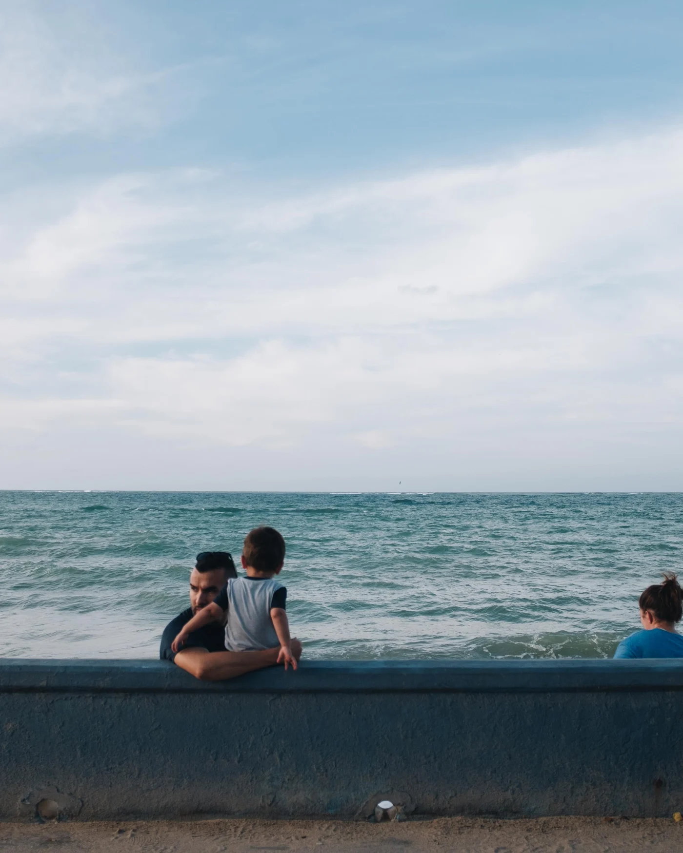 A man lifts a toddler onto a seawall to watch the waves roll in