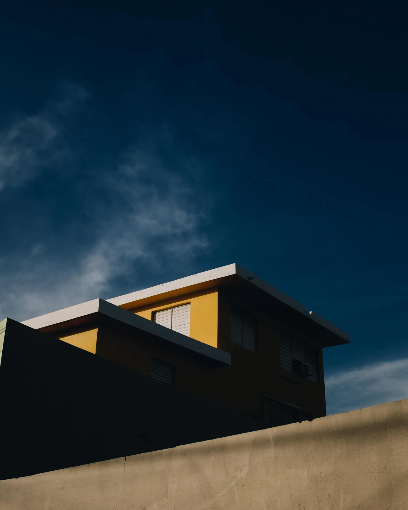 A yellow house catching late sun against a deep blue sky, shadowed wall below