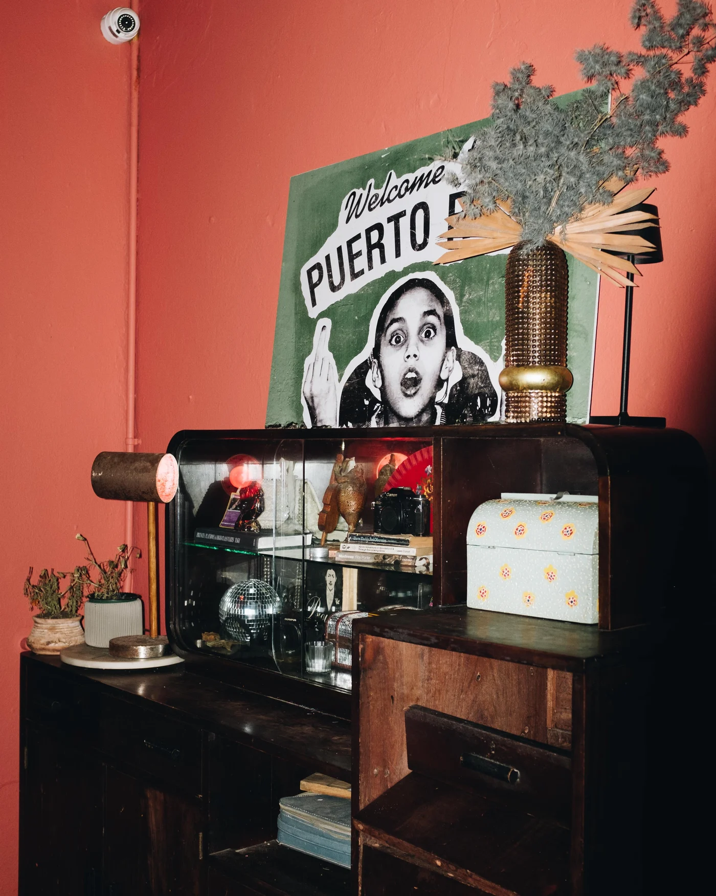 A Welcome Puerto Rico poster above a cluttered vintage cabinet against a coral pink wall
