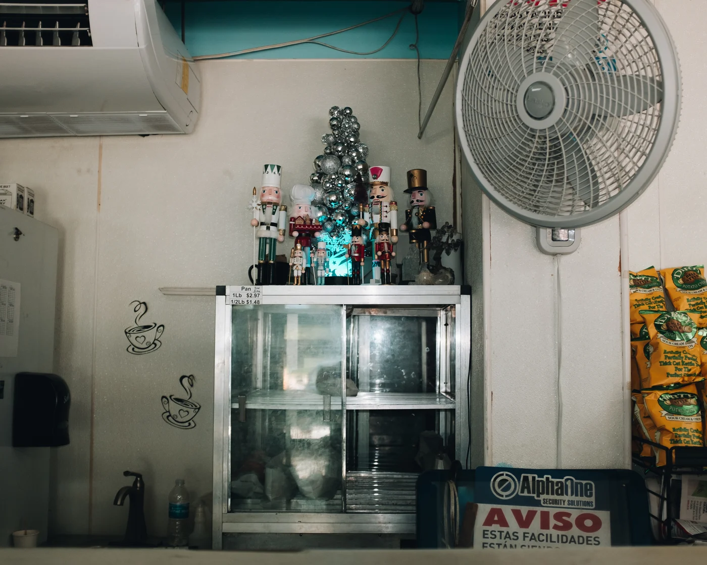 Nutcrackers and a tinsel tree crowd the top of a deli case beside a wall fan