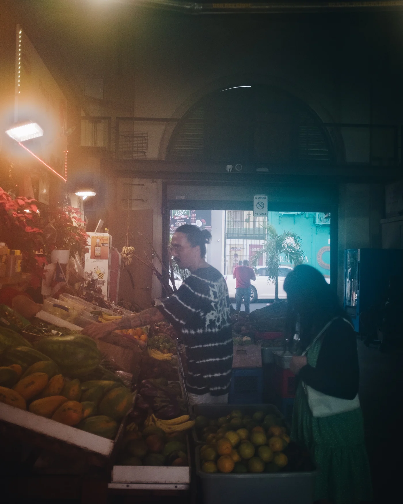 Shoppers picking through papayas and mangoes under the warm lights of a market hall