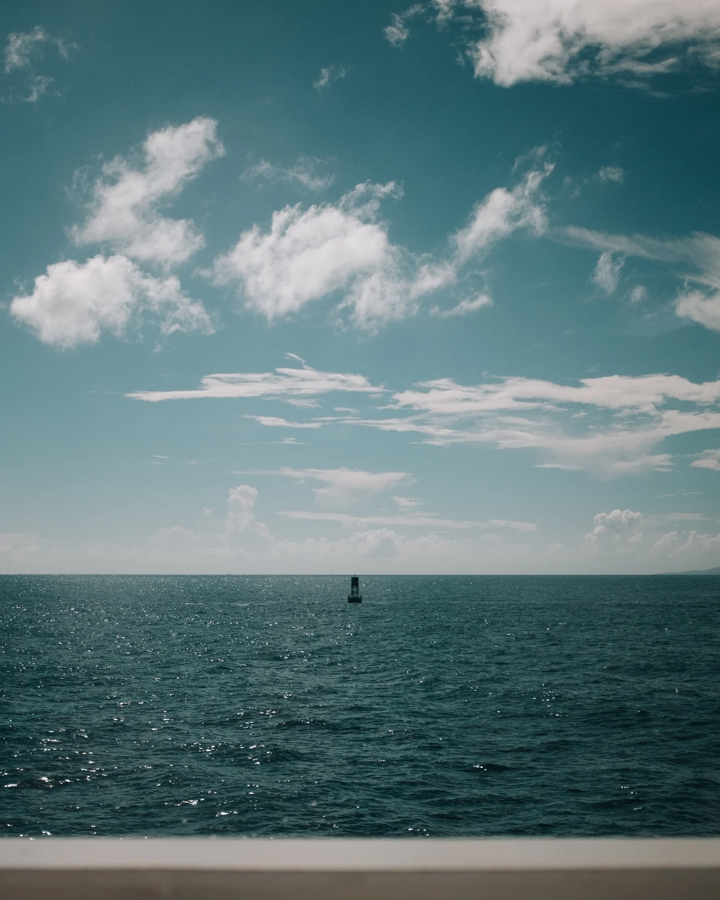 A single buoy adrift in sparkling open water beneath scattered clouds