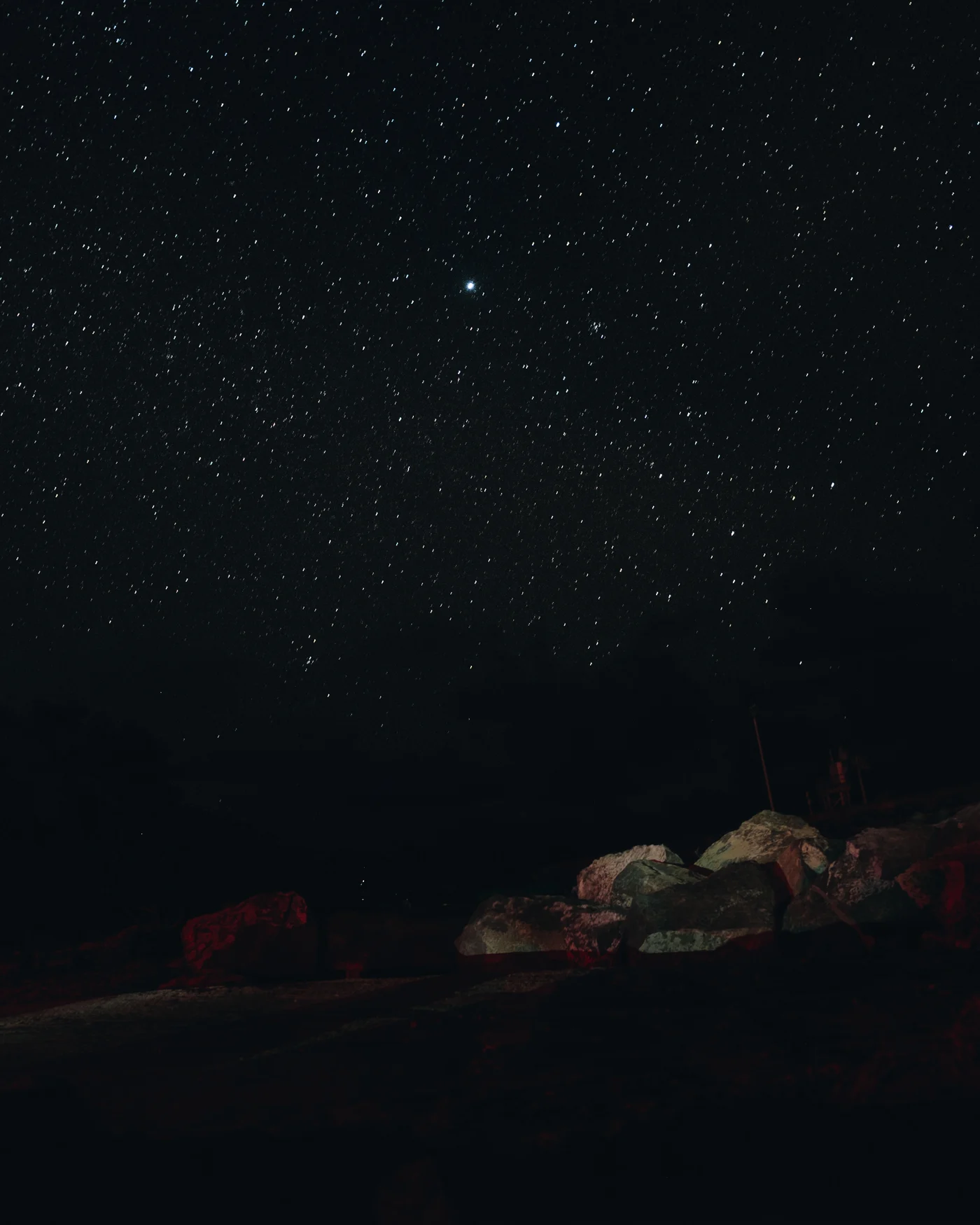 Stars crowding the night sky above boulders faintly lit in red