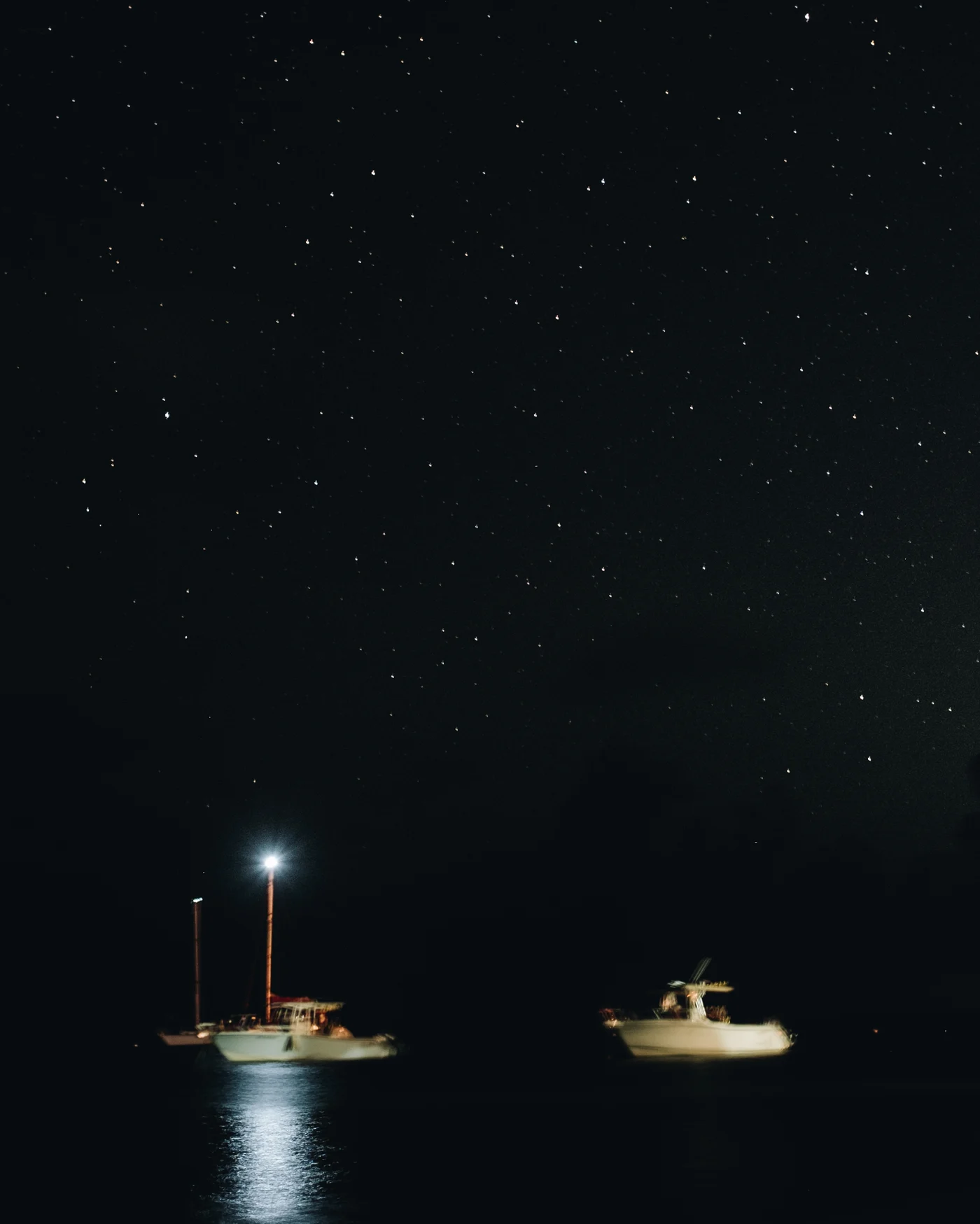 Two small boats at anchor after dark, one masthead light blazing beneath the stars