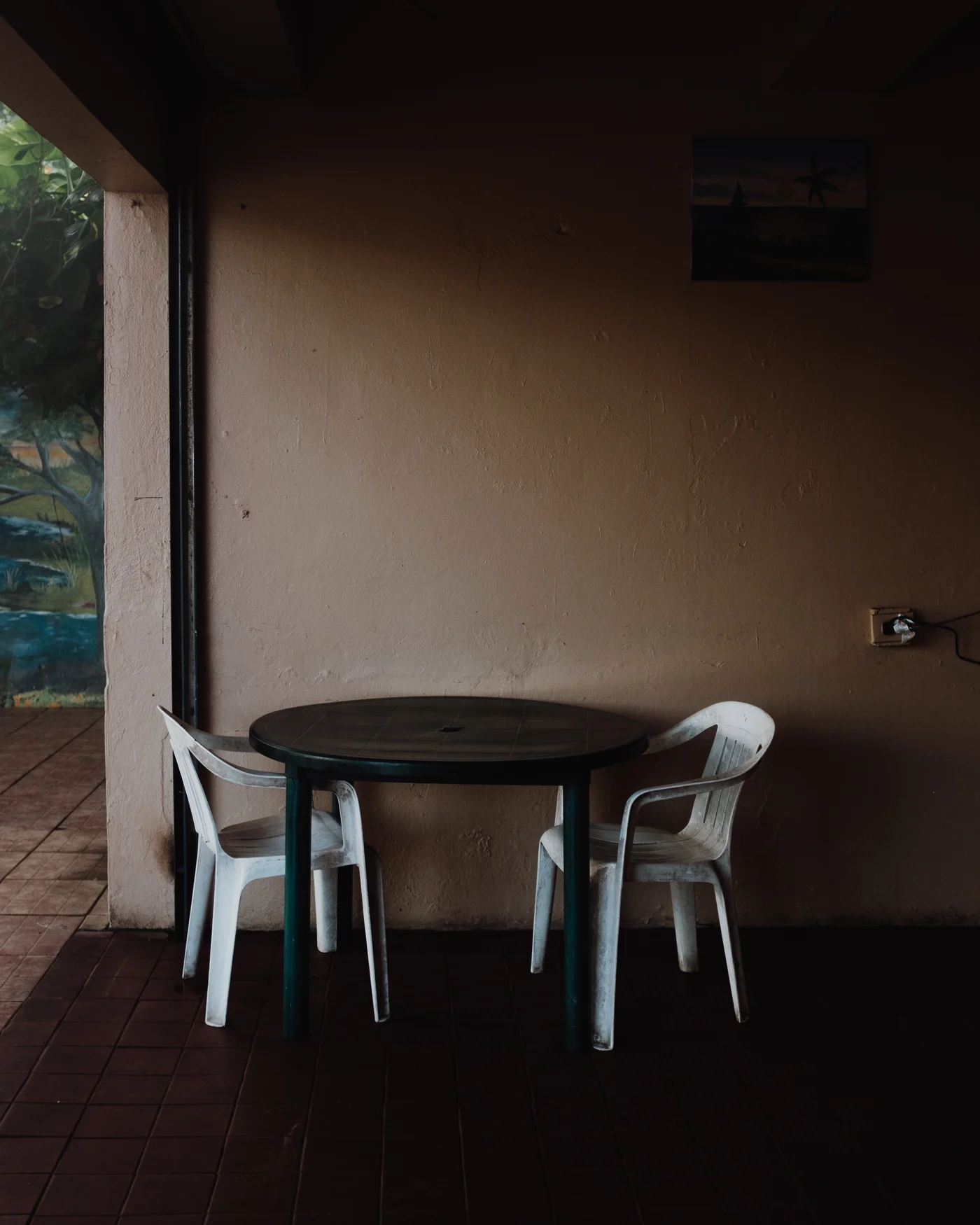 Two white plastic chairs at a dark table on a quiet tiled porch