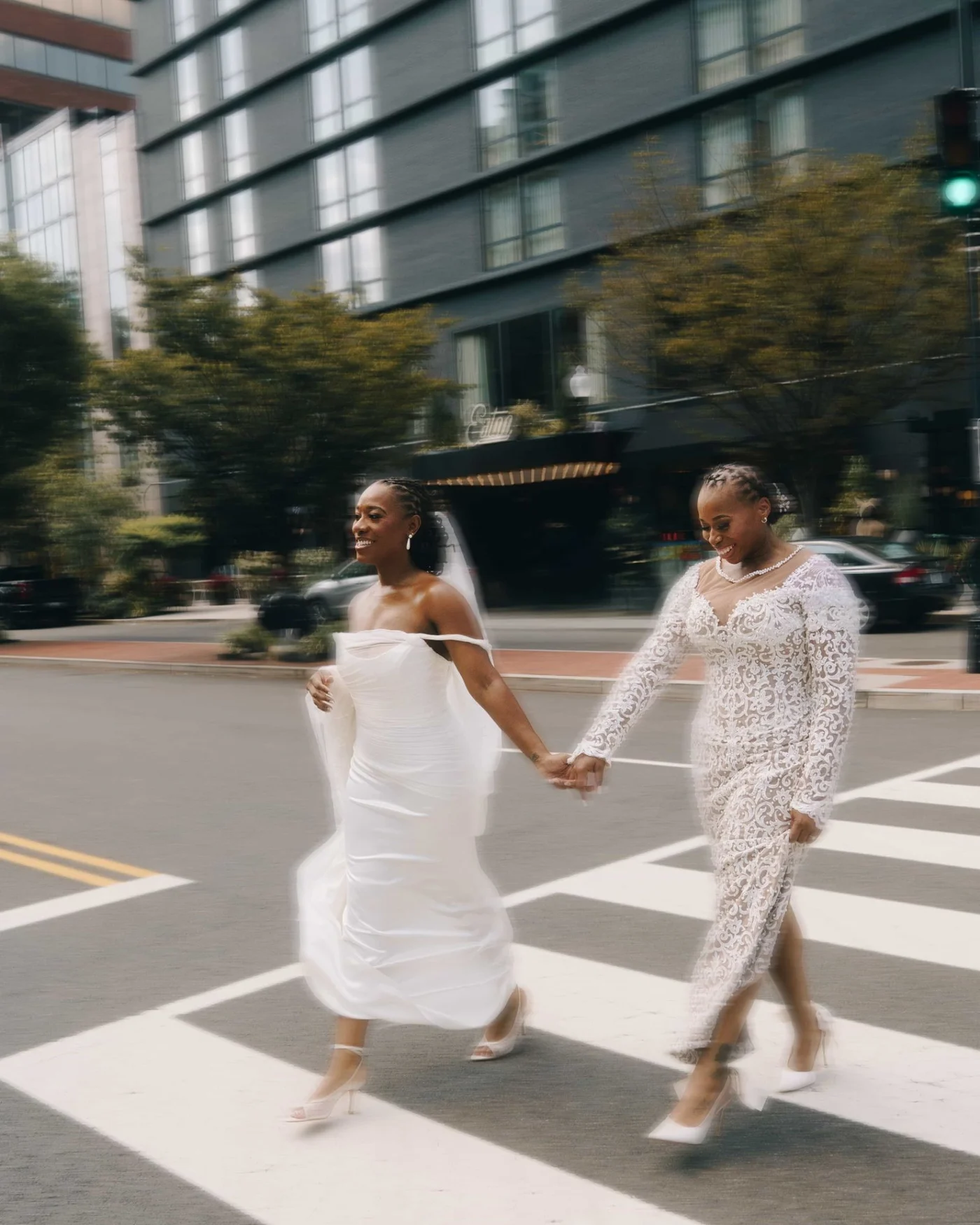 Two brides crossing a city street hand in hand, both blurred with the speed of it