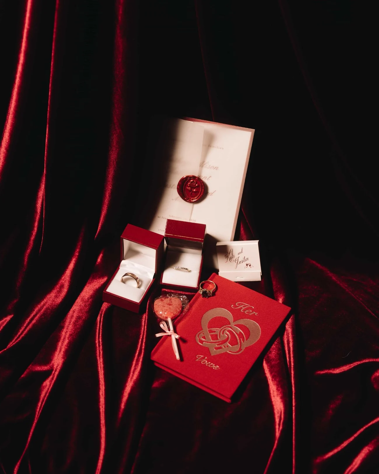 Rings in their boxes on red velvet beside a card printed in gold and a small tasselled knot