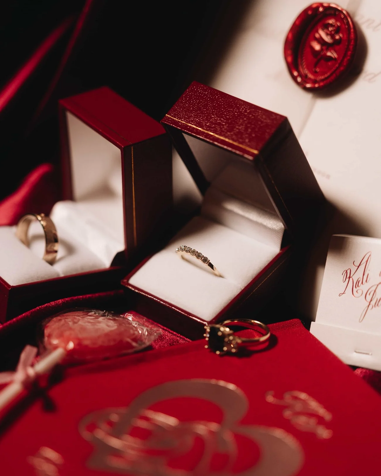 Two gold bands in open boxes on red silk, a round wax seal on the card behind them