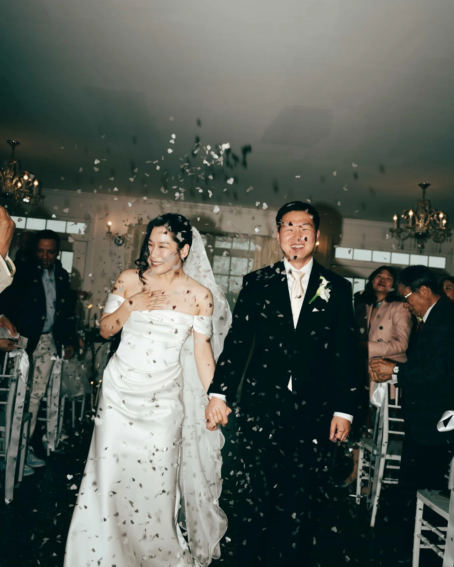 A couple walking back up the aisle through a shower of paper hearts, guests throwing them from both sides
