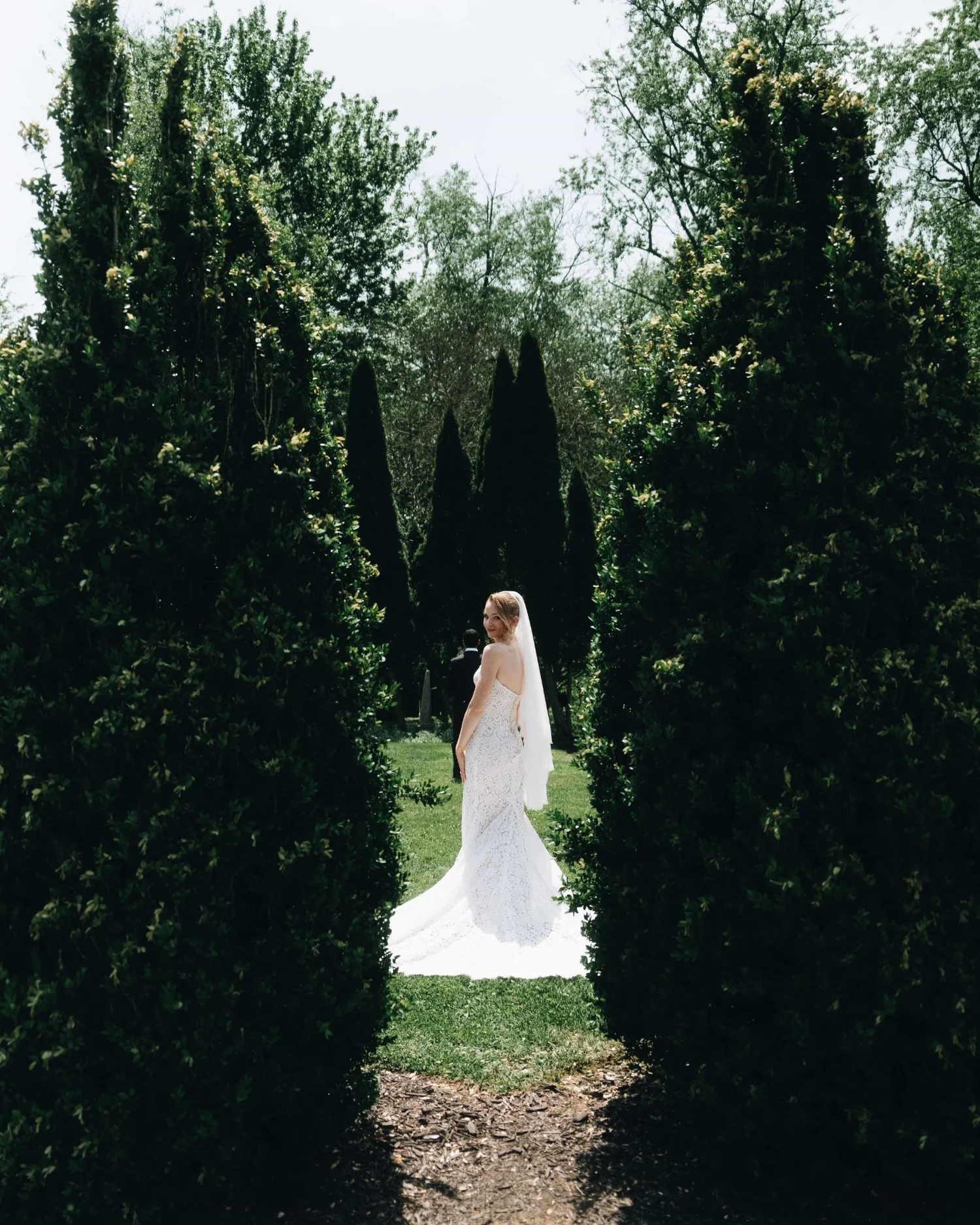A bride standing alone at the end of a corridor of tall clipped hedges